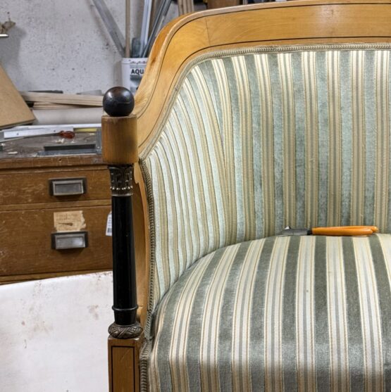 Poltrona in velluto verde sbiadito con dettagli in legno, situata in un atelier con attrezzi sullo sfondo.