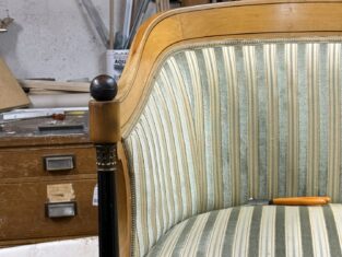 Poltrona in velluto verde sbiadito con dettagli in legno, situata in un atelier con attrezzi sullo sfondo.