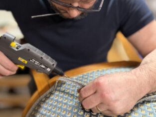 Artigiano che incolla un dettaglio su una poltrona in velluto.
